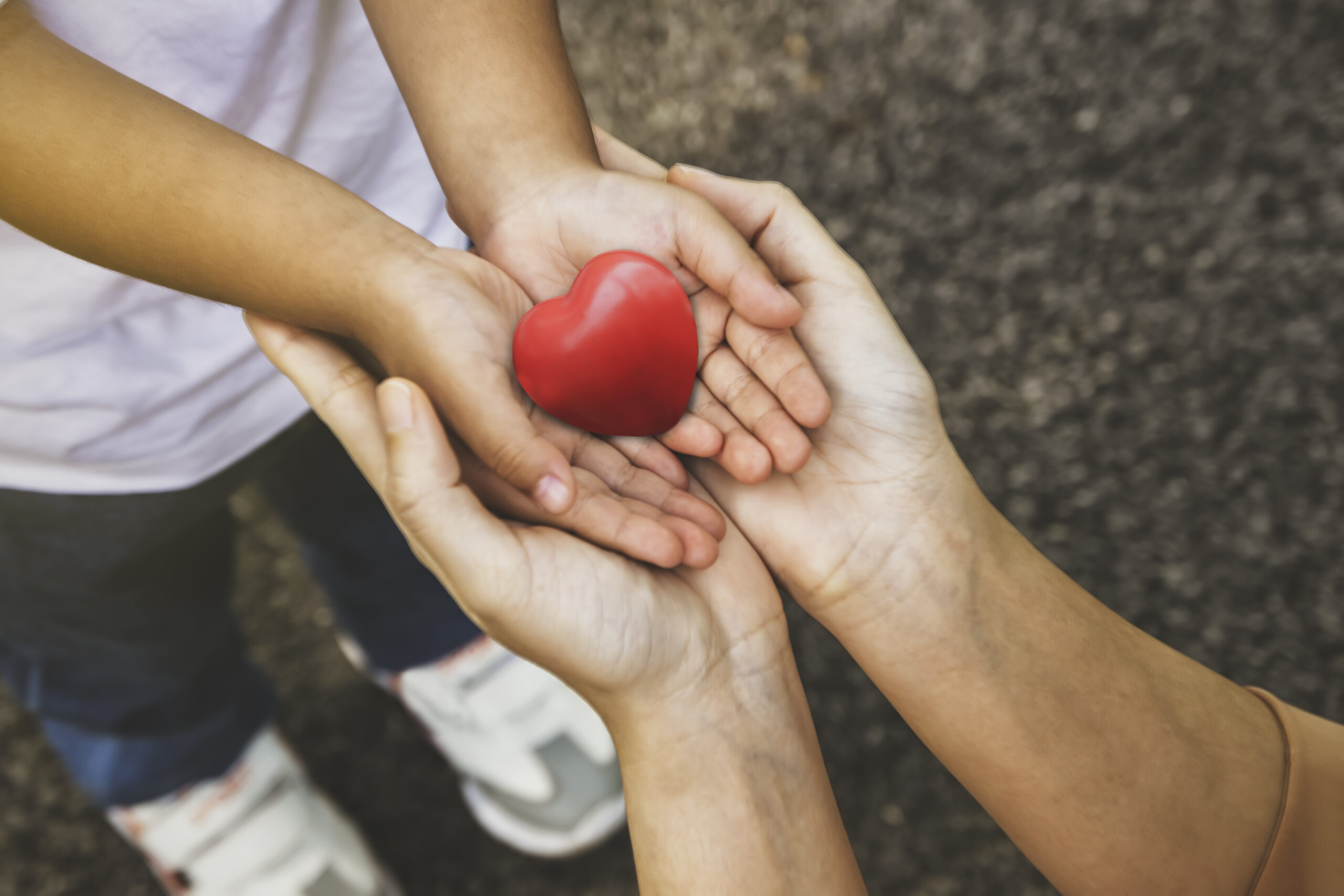 Manos de madre y niño sosteniendo un corazón rojo, representando amor y cuidado familiar.